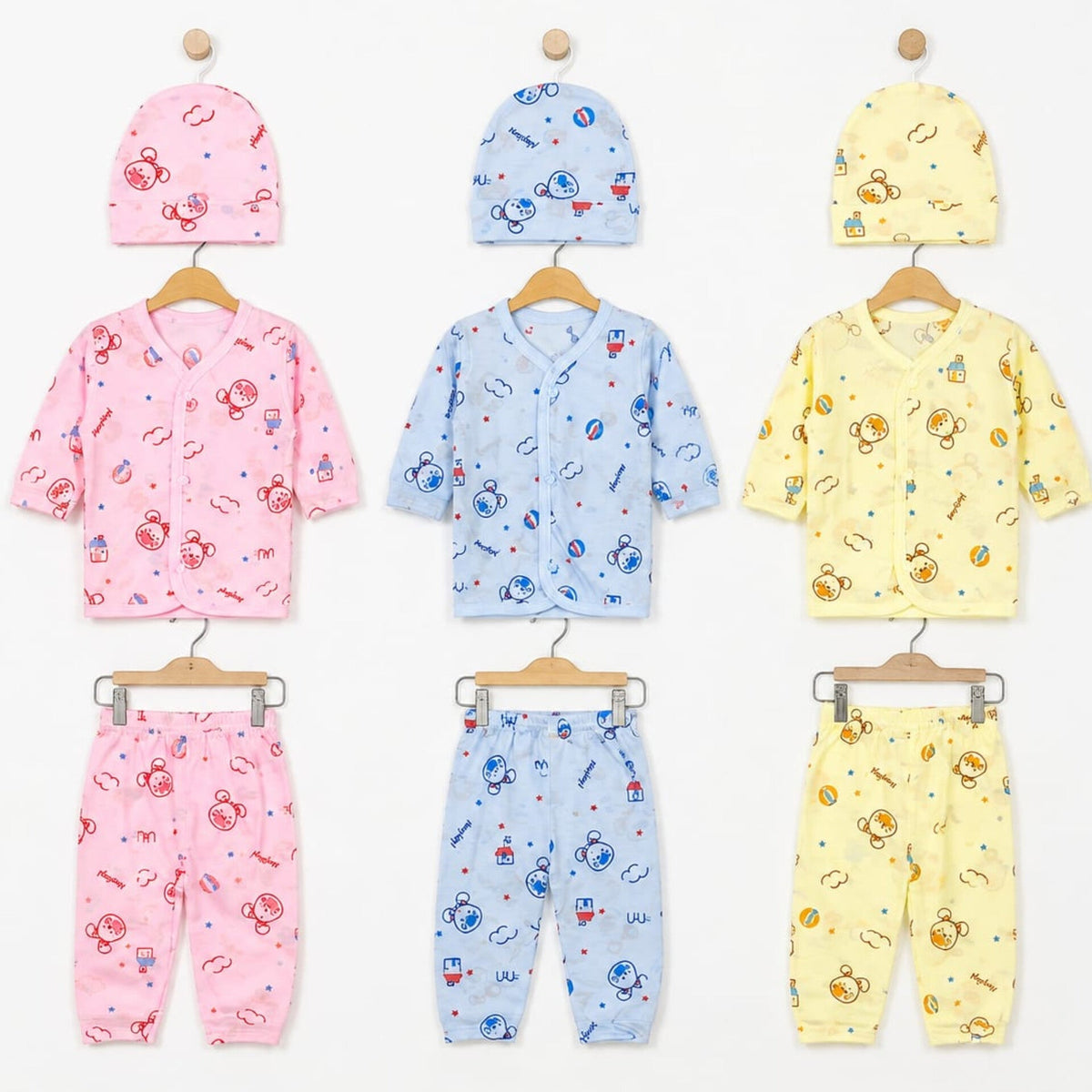 Three baby clothing sets displayed on wooden hangers against a white background, each set including a hat and matching top and pants. The sets are pink, light blue, and pale yellow, all featuring cartoon astronaut prints.