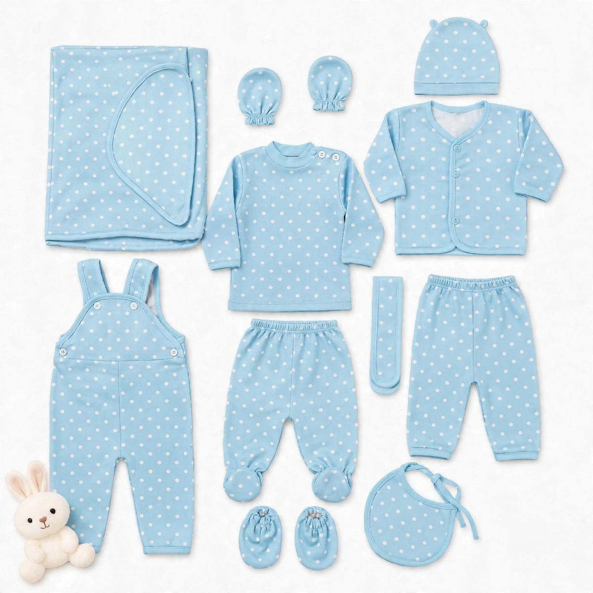 A baby clothing set laid out on a white background, including a light blue long-sleeve top, matching pants, cardigan, hat, bib, booties, overalls, mittens, and a blanket, all with a white polka dot pattern. A small plush bunny is placed at the lower left.