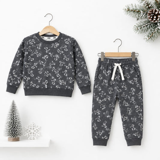 A children's two-piece outfit set consisting of a long-sleeve crewneck sweatshirt and matching jogger pants, both in dark gray with a white snowman pattern, hanging on wooden hangers against a white wall with holiday decorations.