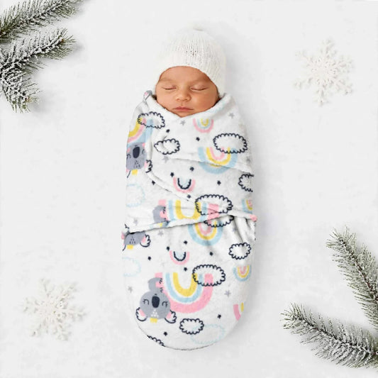 A sleeping newborn baby wrapped in a white swaddle blanket with a colorful cartoon rainbow and cloud pattern, wearing a white knit hat, styled on a white background with snowflake decorations and pine branches.