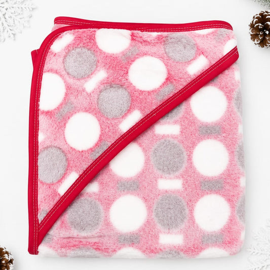 A folded plush hooded blanket in pink, white, and gray with a red border, photographed on a white background with small decorative holiday props in the corners.