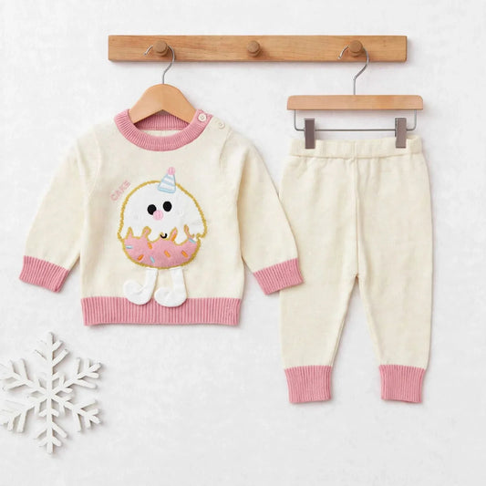 A baby knit two-piece outfit set consisting of a cream sweater with pink ribbed trim and a cute donut character applique, paired with matching cream pants with pink ribbed cuffs, displayed on wooden hangers against a light background.