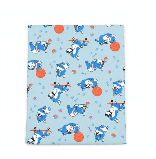 A square fabric item, likely a blanket or towel, featuring a light blue background with a playful pattern of cartoon French bulldogs rolling up their blue and white sweaters, alongside orange basketballs, pink stars, and small rainbow accents.