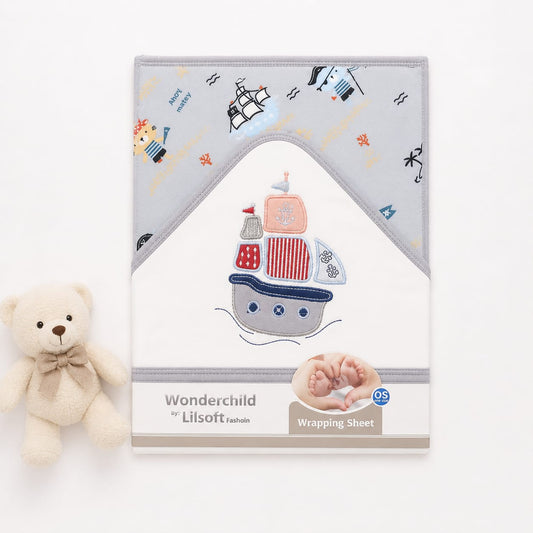 A baby wrapping sheet with a nautical theme, displayed next to a small cream teddy bear. The sheet features a light gray top section with embroidered ships, waves, and stars, and a white bottom section with a large embroidered ship design.