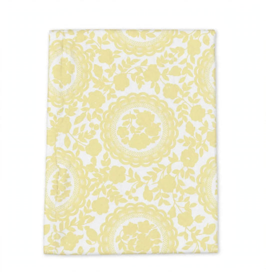 A rectangular white fabric item, likely a tea towel or napkin, featuring a repeating light yellow floral and circular lace-like pattern, shown flat against a white background.