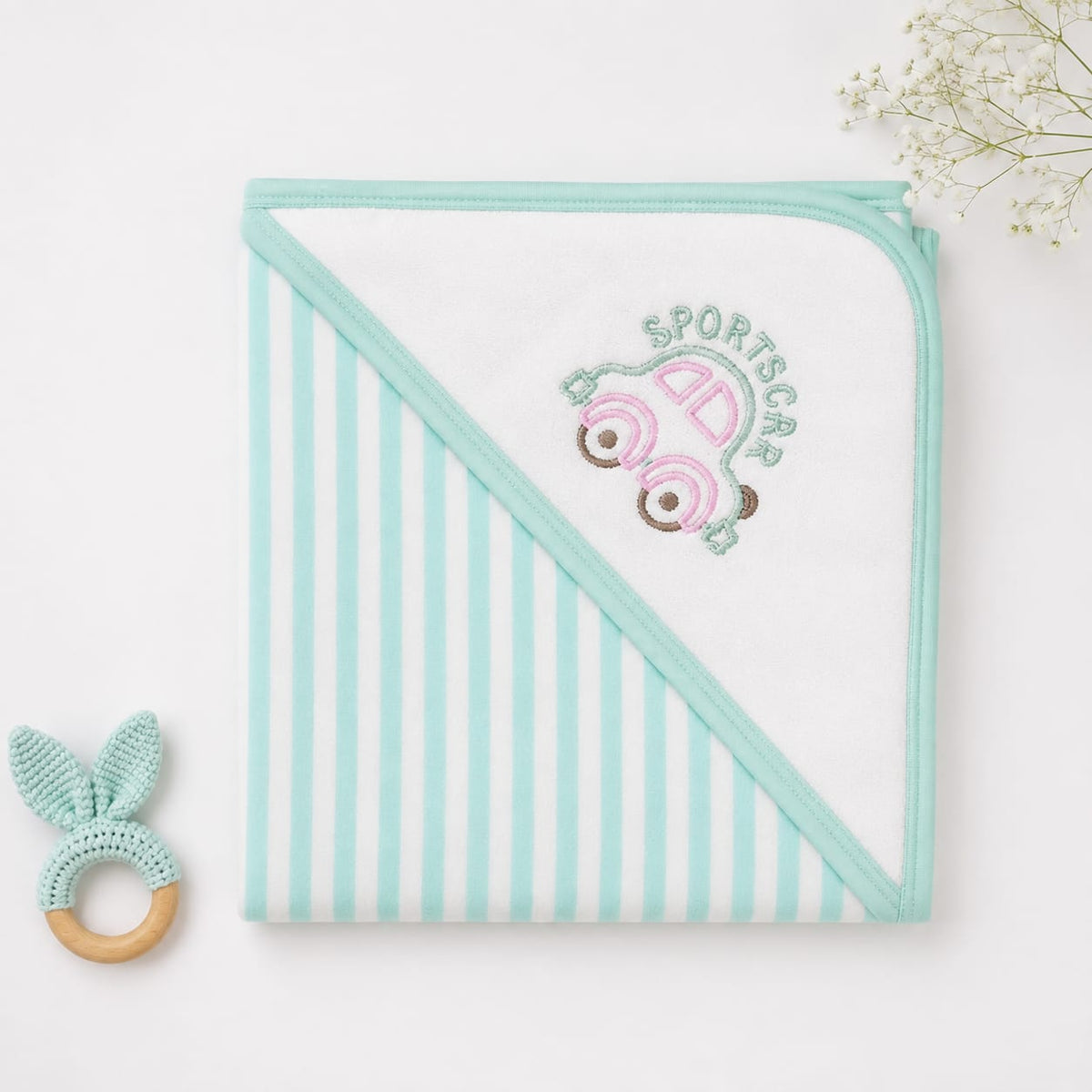 A folded baby hooded towel with mint green and white vertical stripes on one side and a solid mint green border, featuring an embroidered pink sports car and the words 'SPORTSCAR' on the corner. A small mint and wooden teething ring is placed to the left 